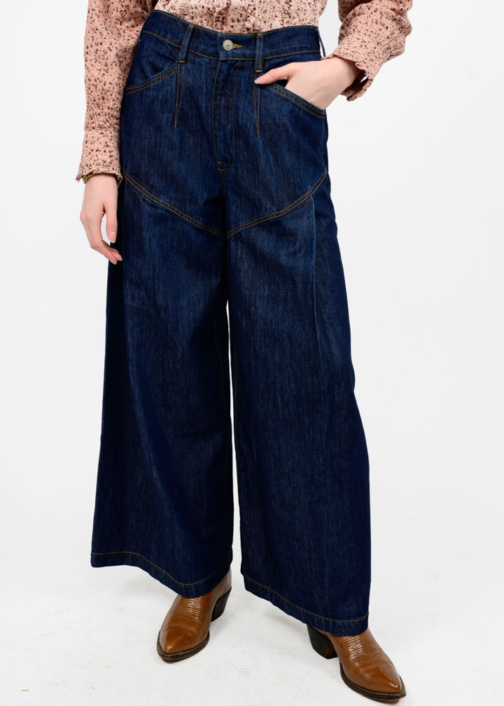 Woman wearing dark blue wide leg jeans with brown boots in front of a white background