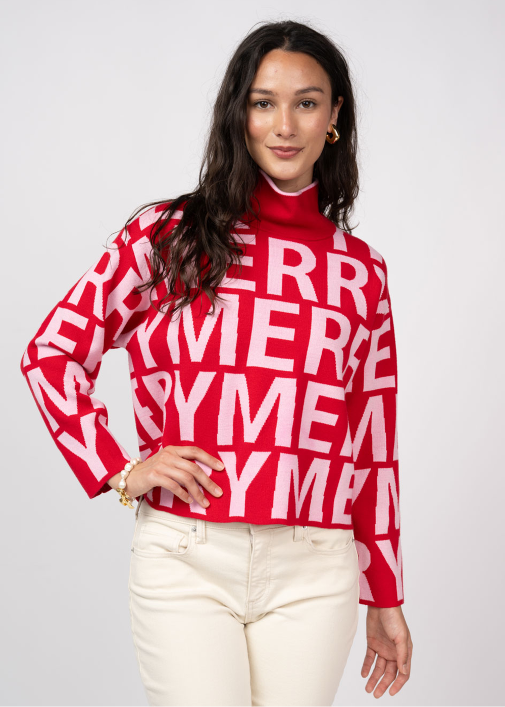 Woman wearing a red mock neck sweater with white "MERRY" letters and white jeans 