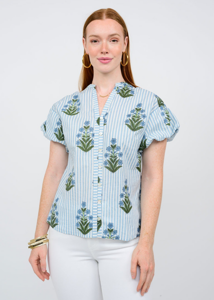 A woman wearing a blue and white striped button down top with puff sleeves and blue floral designs in from of a white background