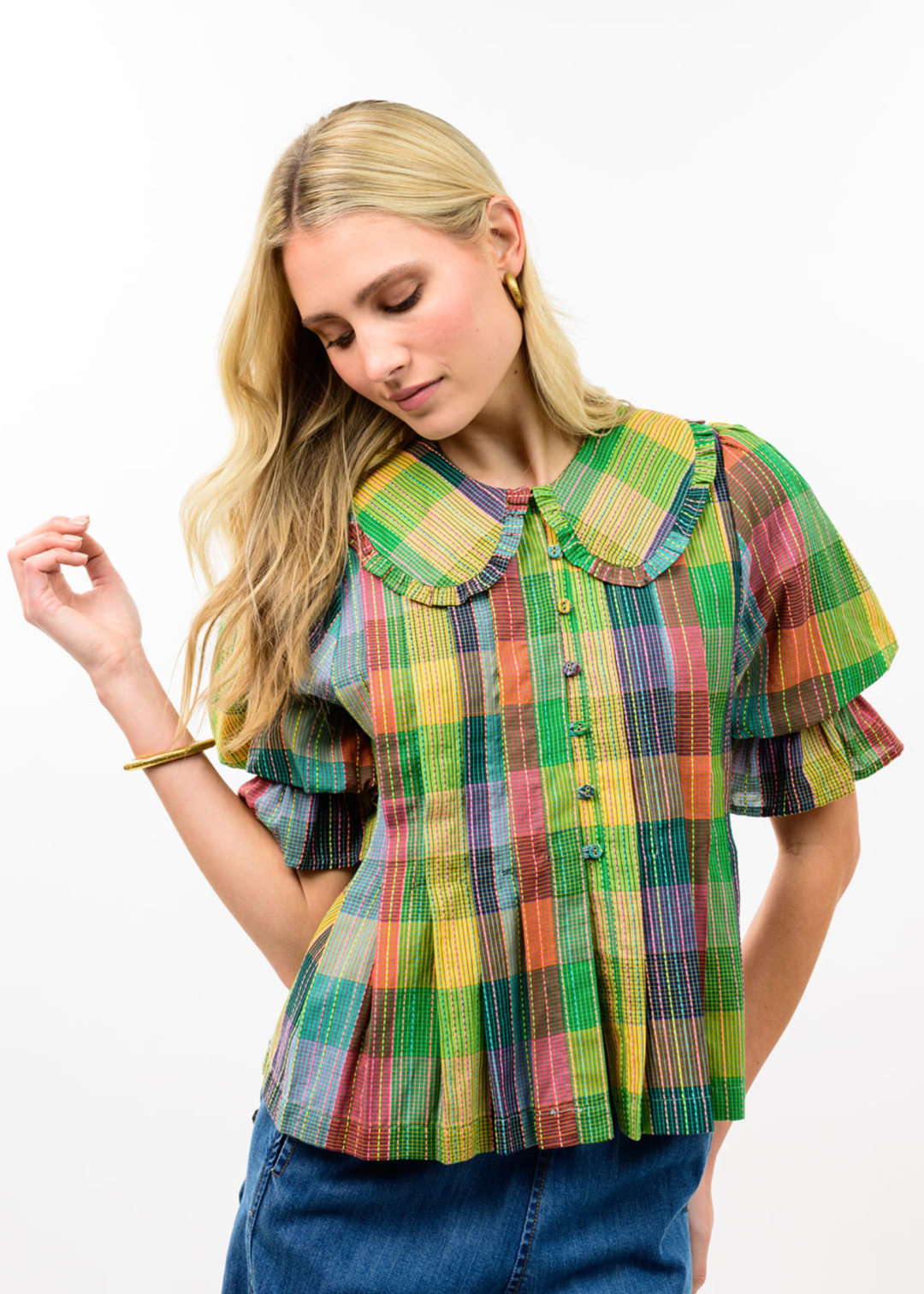 Woman wearing a multicolor plaid top with dark blue jeans against a white background