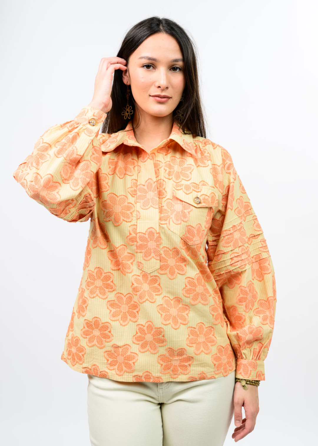 Woman wearing an orange and yellow floral collared top with tan pants