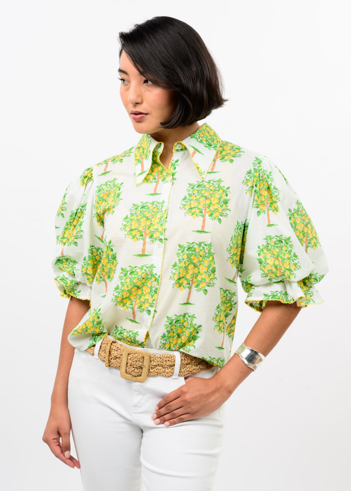 Woman wearing a white button down with a lemon tree graphic print and white pants