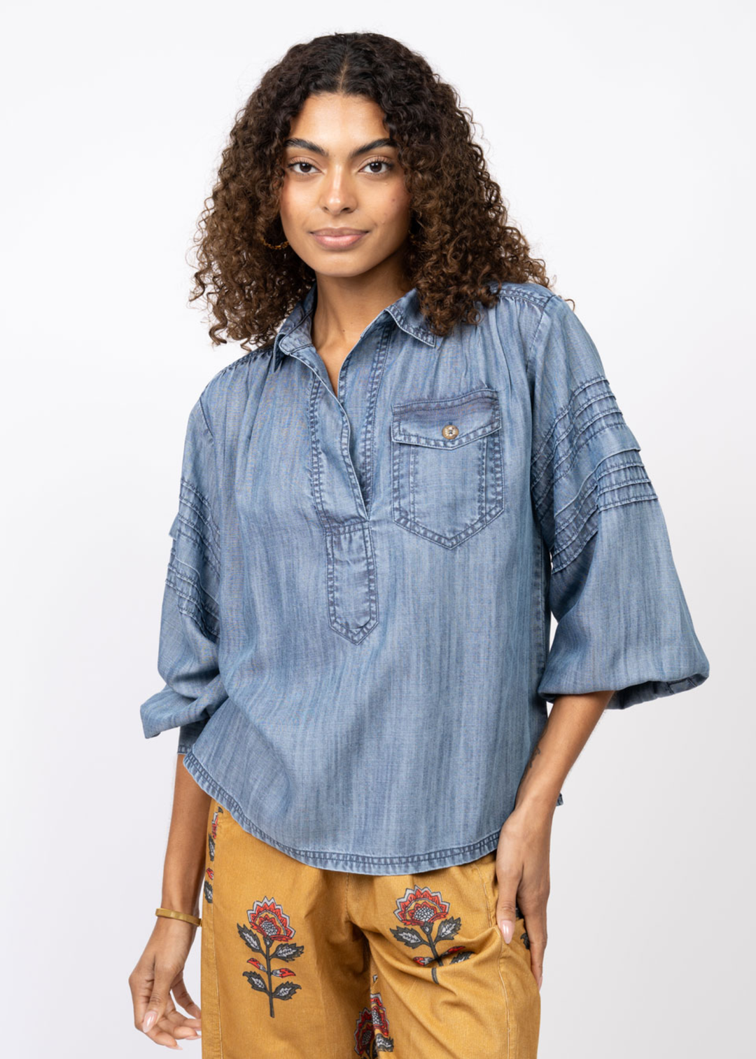 Woman wearing a denim collared shirt with yellow floral pants in front of a white background