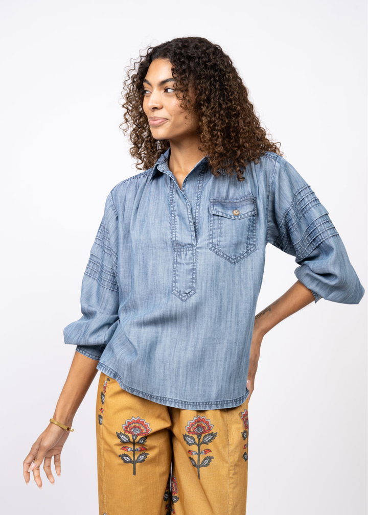 Woman wearing a denim collared shirt with yellow floral pants in front of a white background