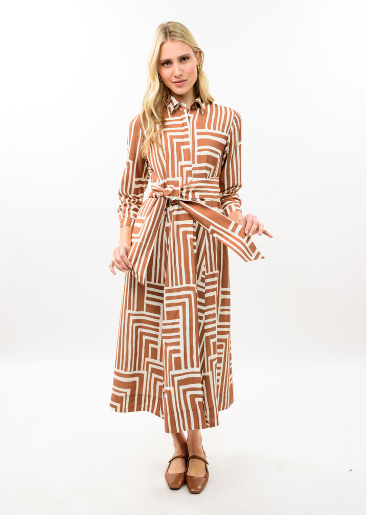 Woman wearing brown midi dress with collar and belt. It has white square patterns on it. 