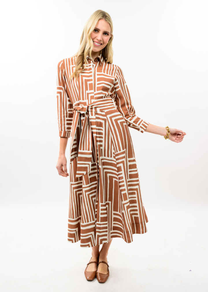 Woman wearing brown midi dress with collar and belt. It has white square patterns on it. 
