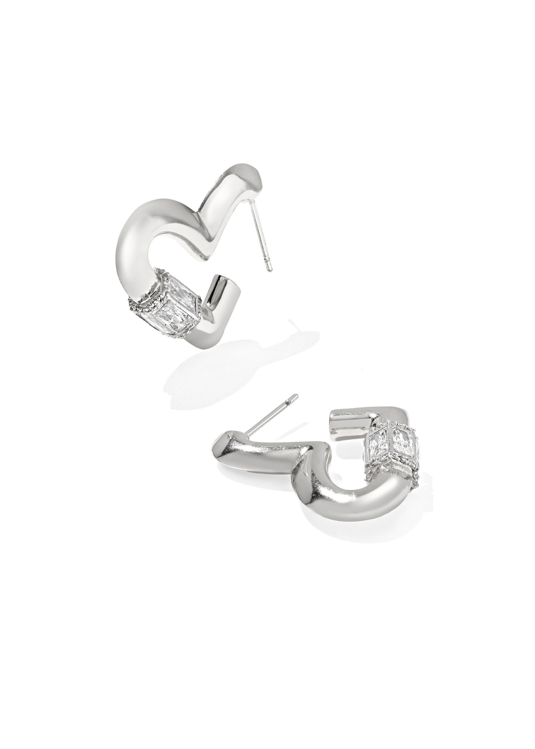 A pair of rhodium heart shaped hoop earrings with CZ details laying on a white background