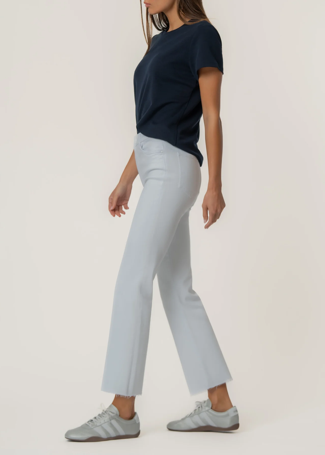 Woman turned to the side wearing a white flare jean with a t-shirt and sneakers