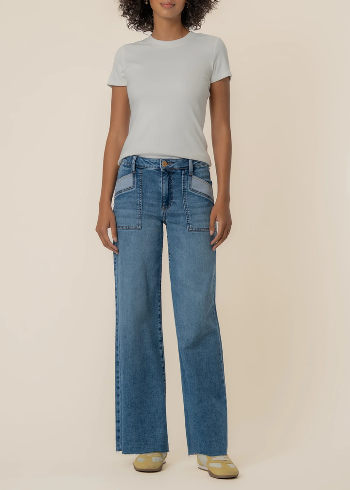 Woman wearing blue wide leg jeans with a raw hem and front pockets against a tan background
