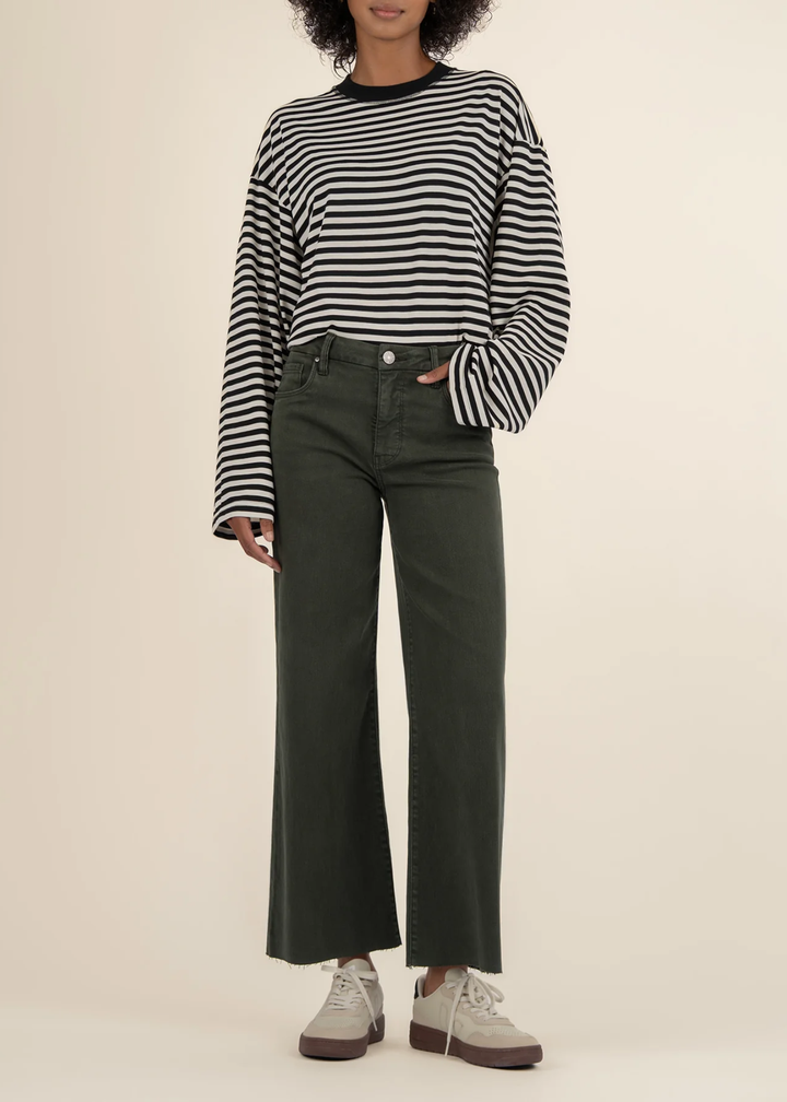 Woman wearing dark green jeans with a black and white striped sweater and white sneakers in front of a white background