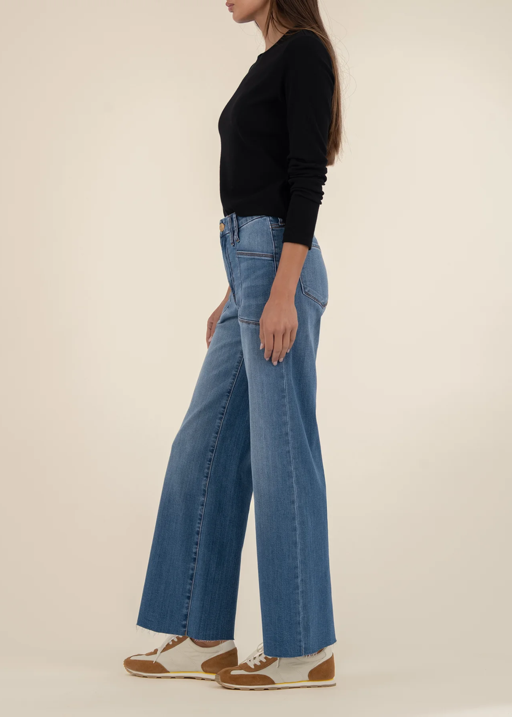 Woman turned to the side wearing medium wash wide leg jeans with a long sleeve back top and brown and white sneakers