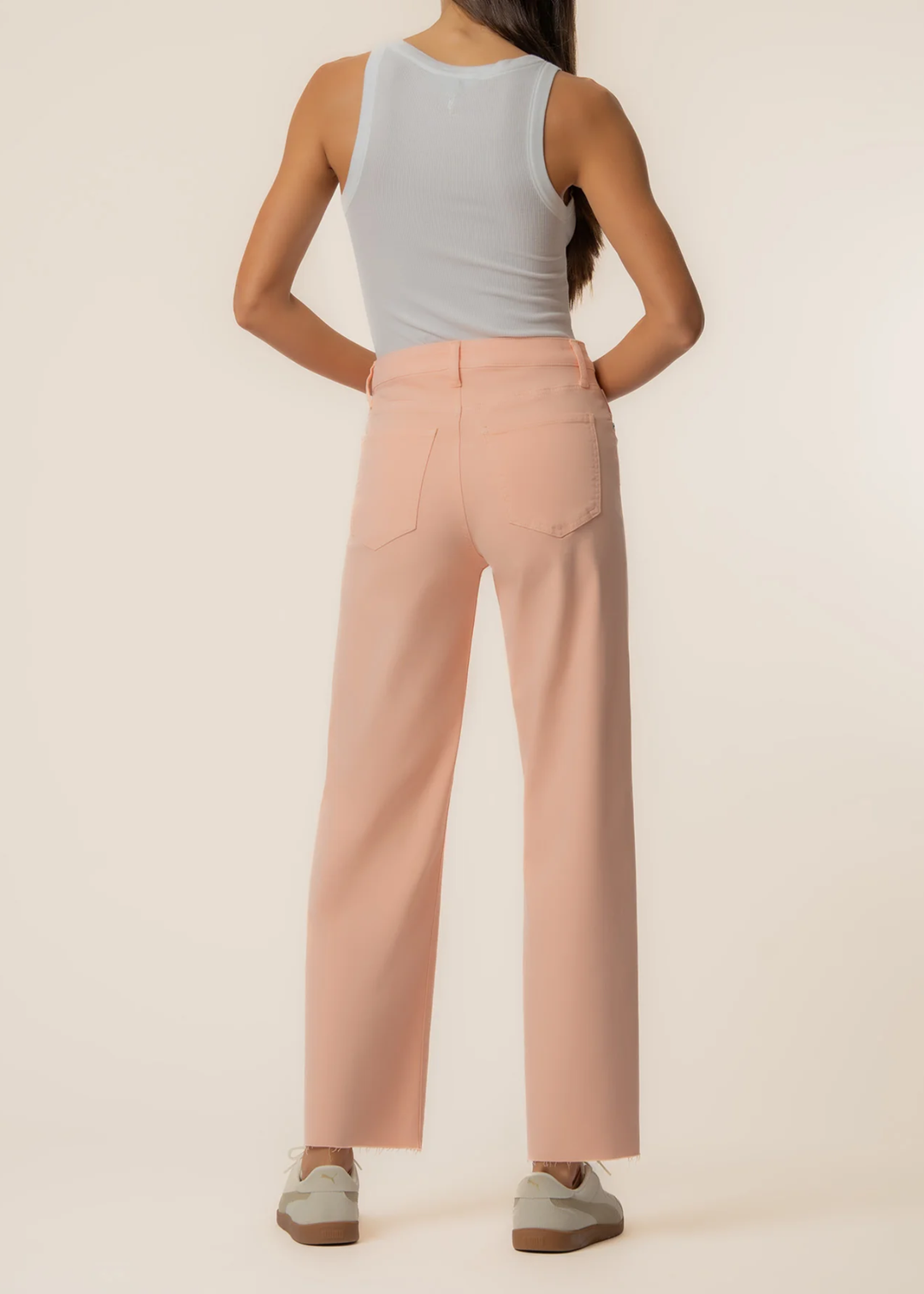 Woman turned around wearing orange wide leg jeans with a grey tank and sneakers