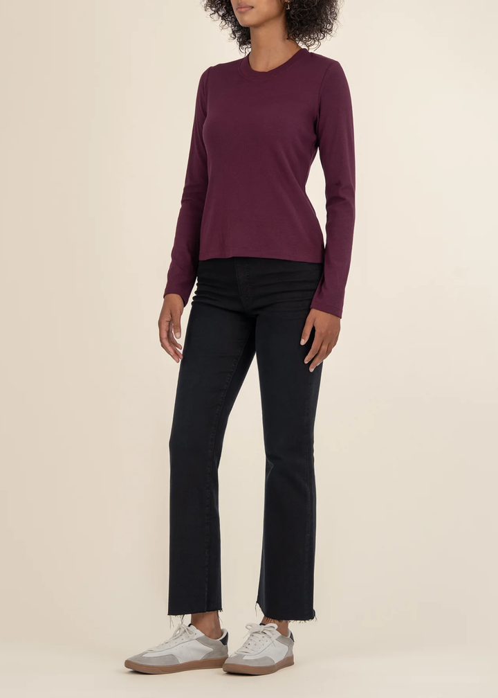 Woman turned to the side wearing a maroon long sleeve tee with black jeans and white sneakers in front of a white background