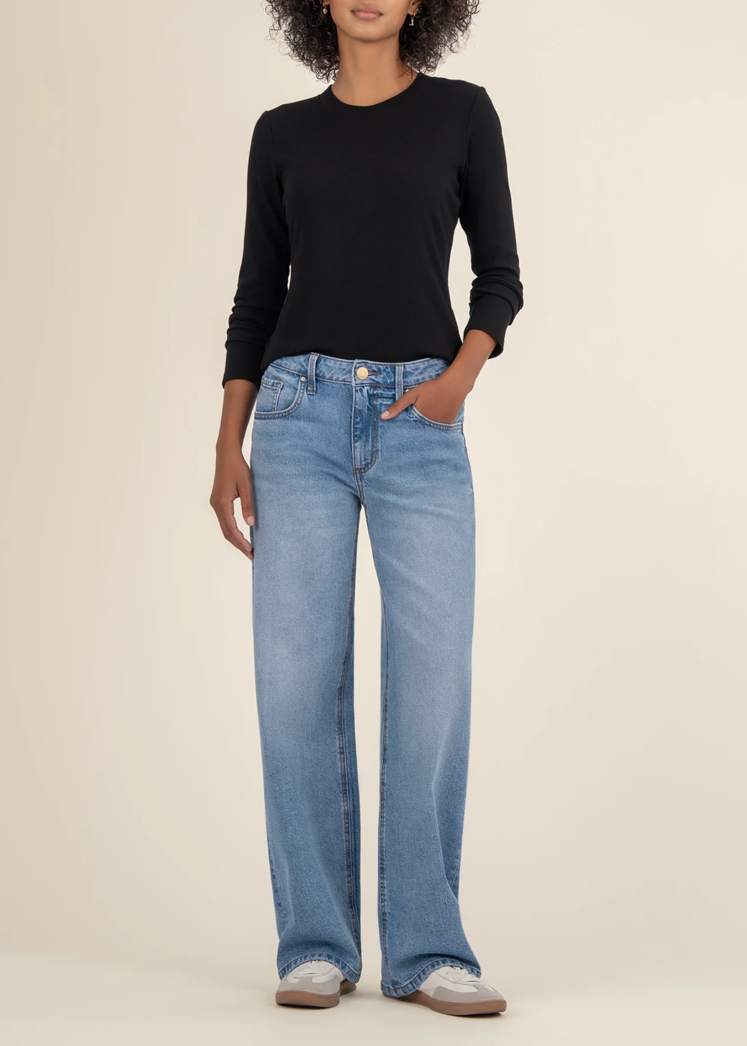 Woman wearing a black long sleeve tee with jeans and white sneakers in front of a white background