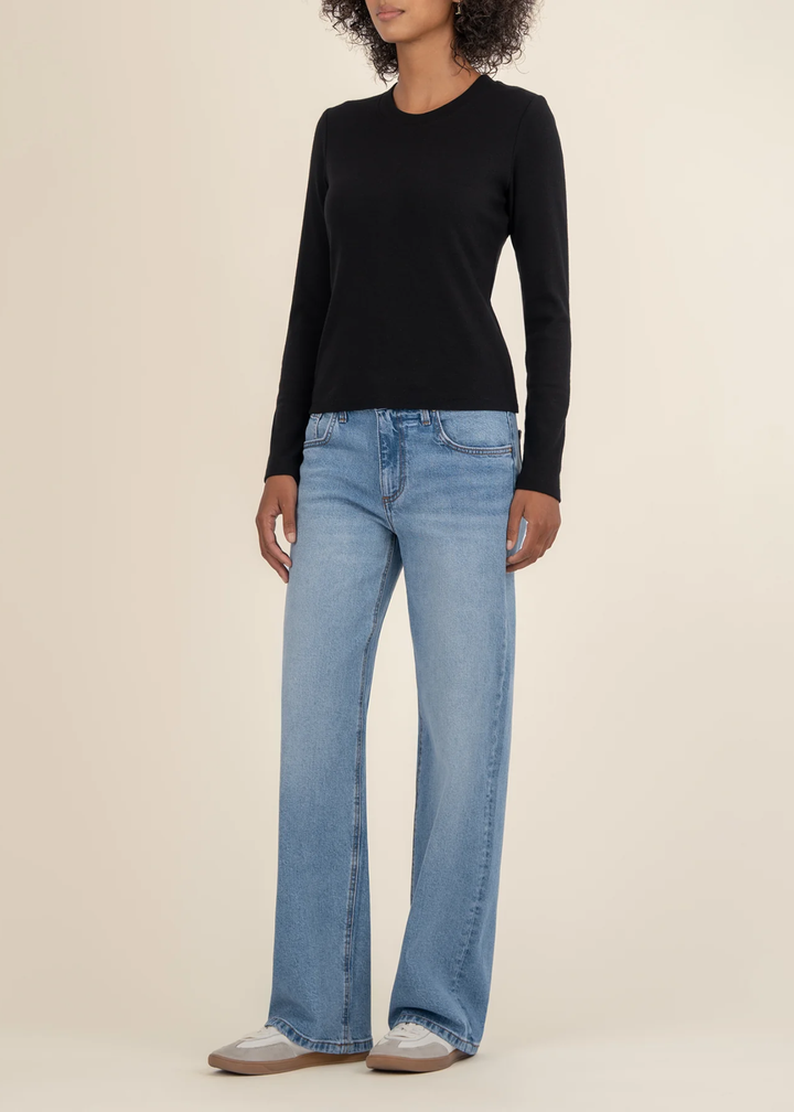 Woman turned to the side wearing a black long sleeve tee with jeans and white sneakers in front of a white background