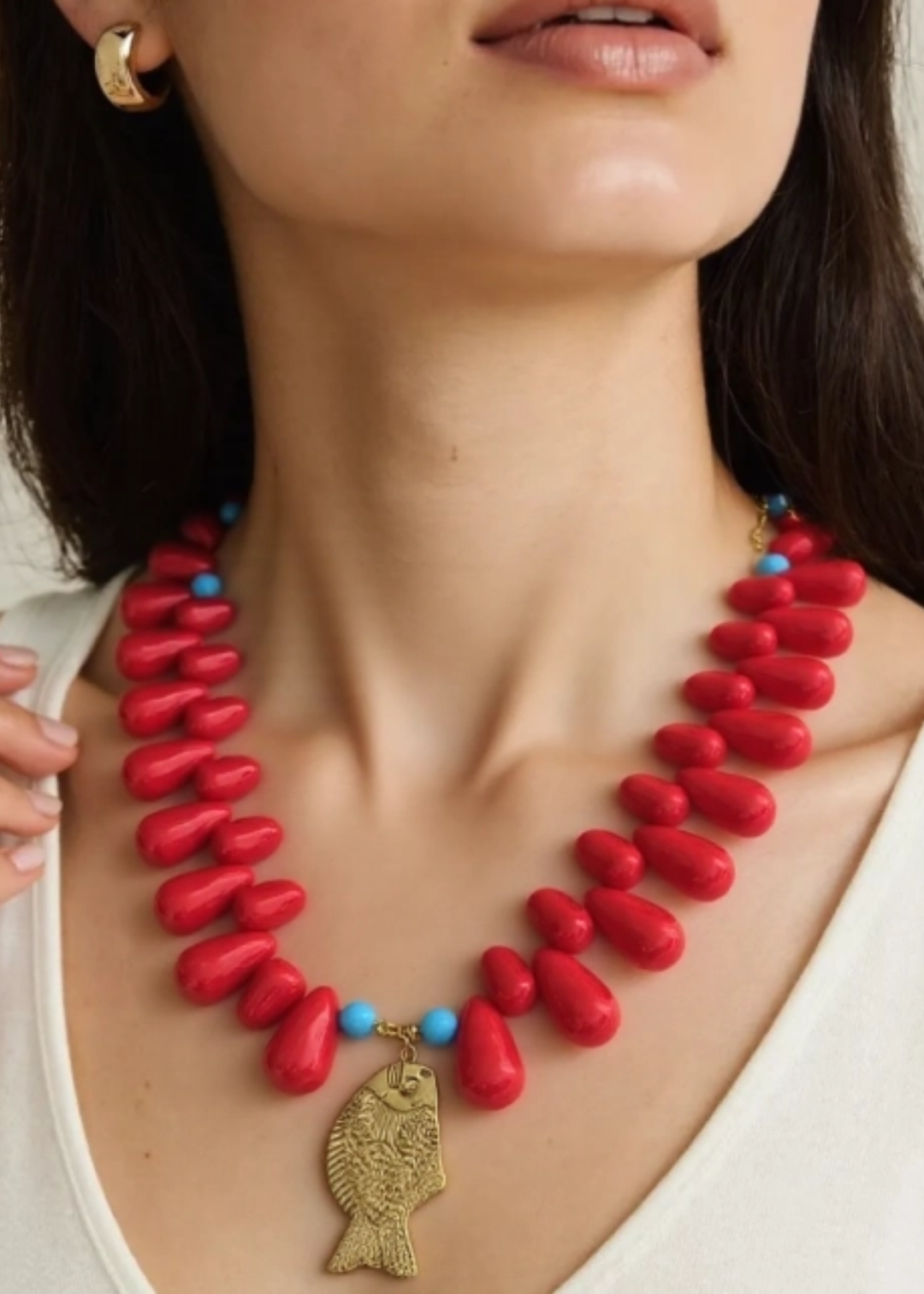 Woman wearing a red beaded necklace with a gold fish charm