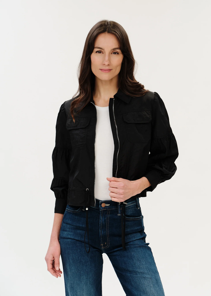Woman with dark hair posing in black jacket with hand on the zipper.