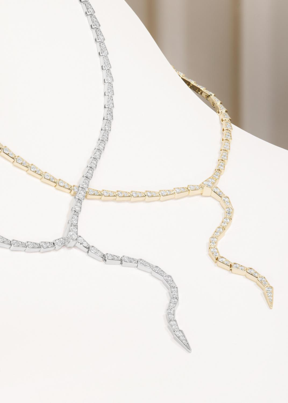 Gold and silver lariat necklaces with simulated diamonds on a white background
