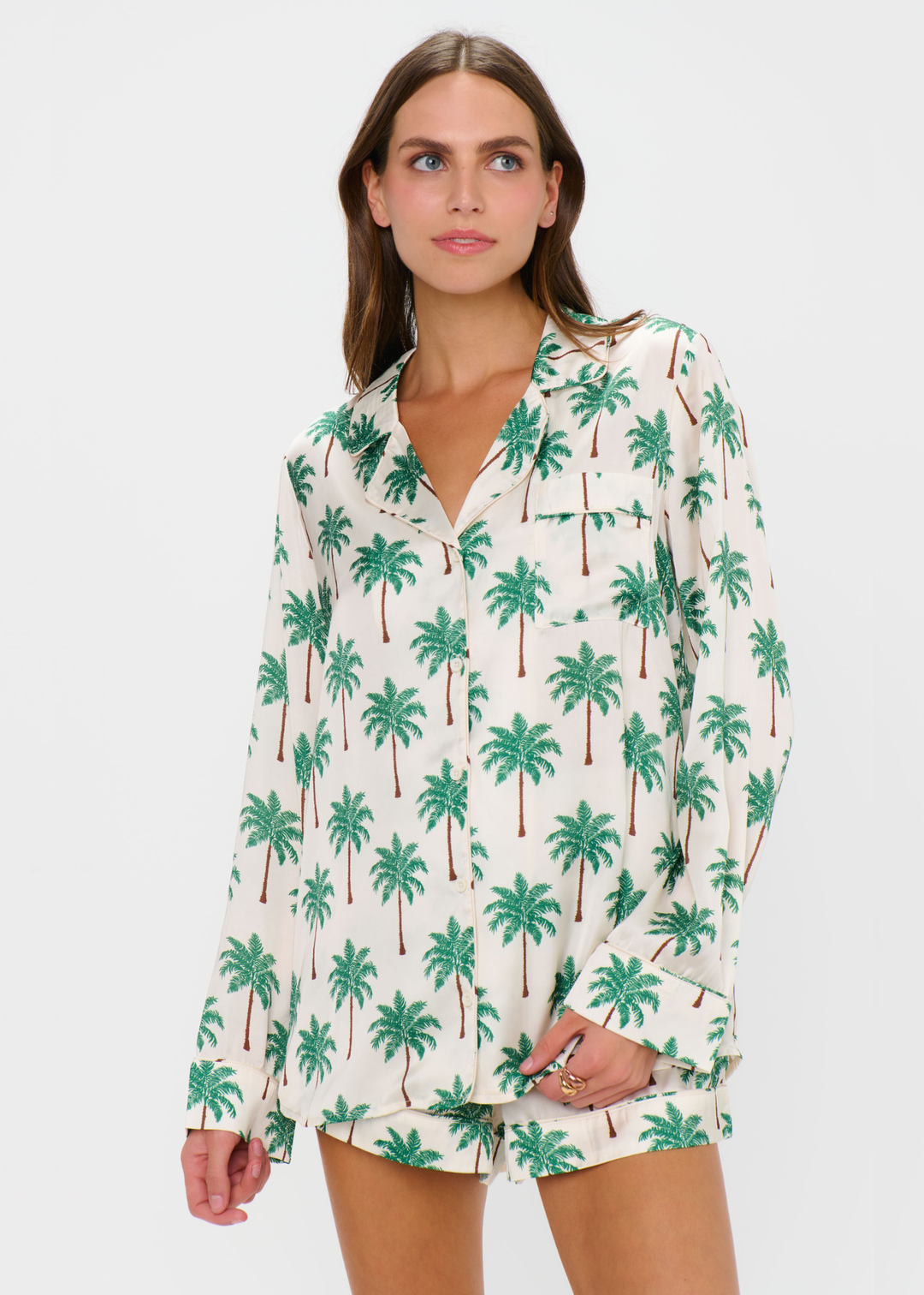 Woman wearing a palm tree patterned pajama set with shorts and a long sleeve top against a white background