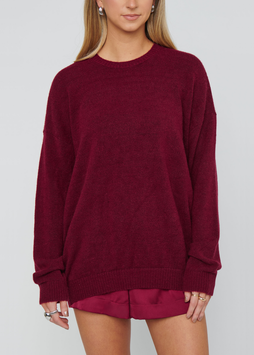 Woman wearing a maroon knit sweater in front of a grey background