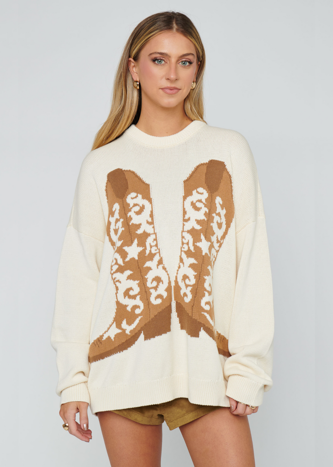 Woman wearing a white sweater with a brown cowboy boot graphic
