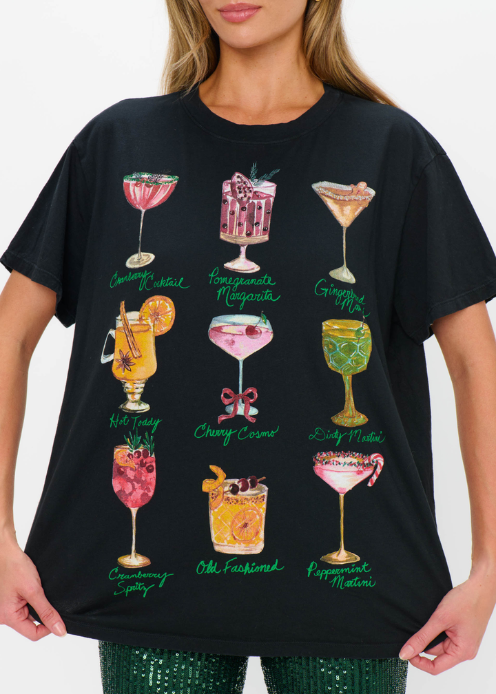 Close up of a woman wearing a black cocktails graphic tee with green sequin pants against a white background