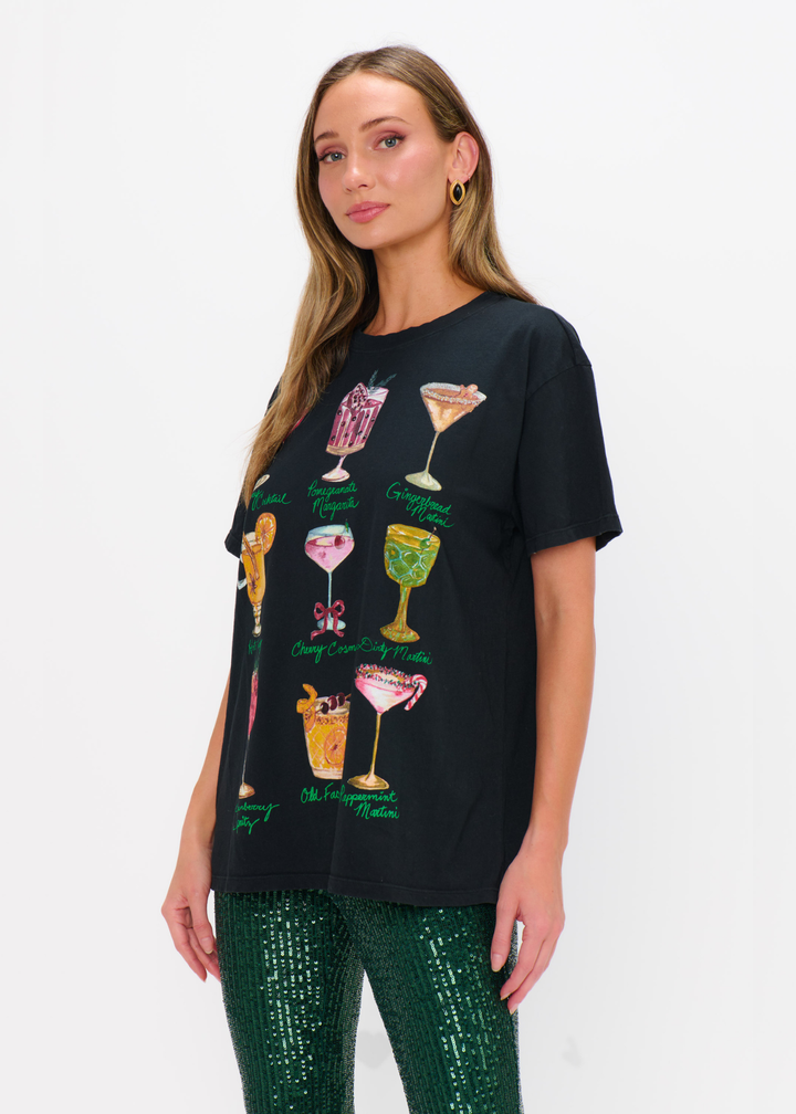 Woman wearing a black cocktails graphic tee with green sequin pants against a white background