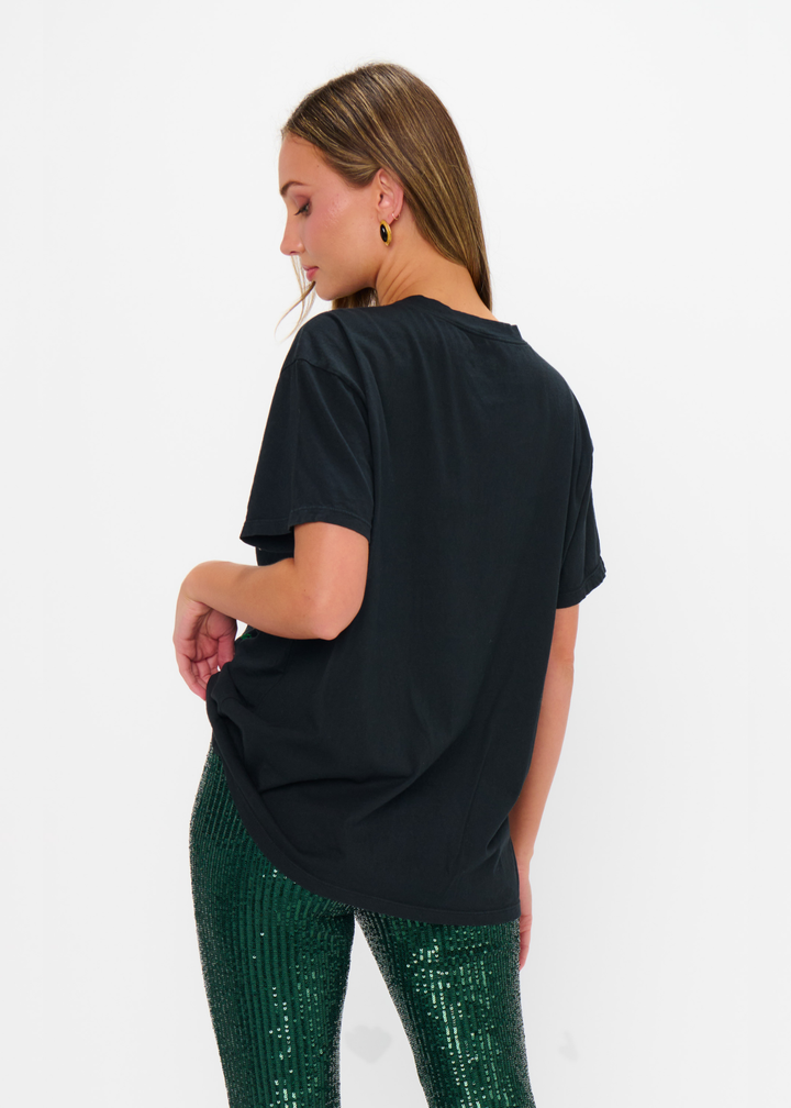 Woman turned around wearing a black cocktails graphic tee with green sequin pants against a white background
