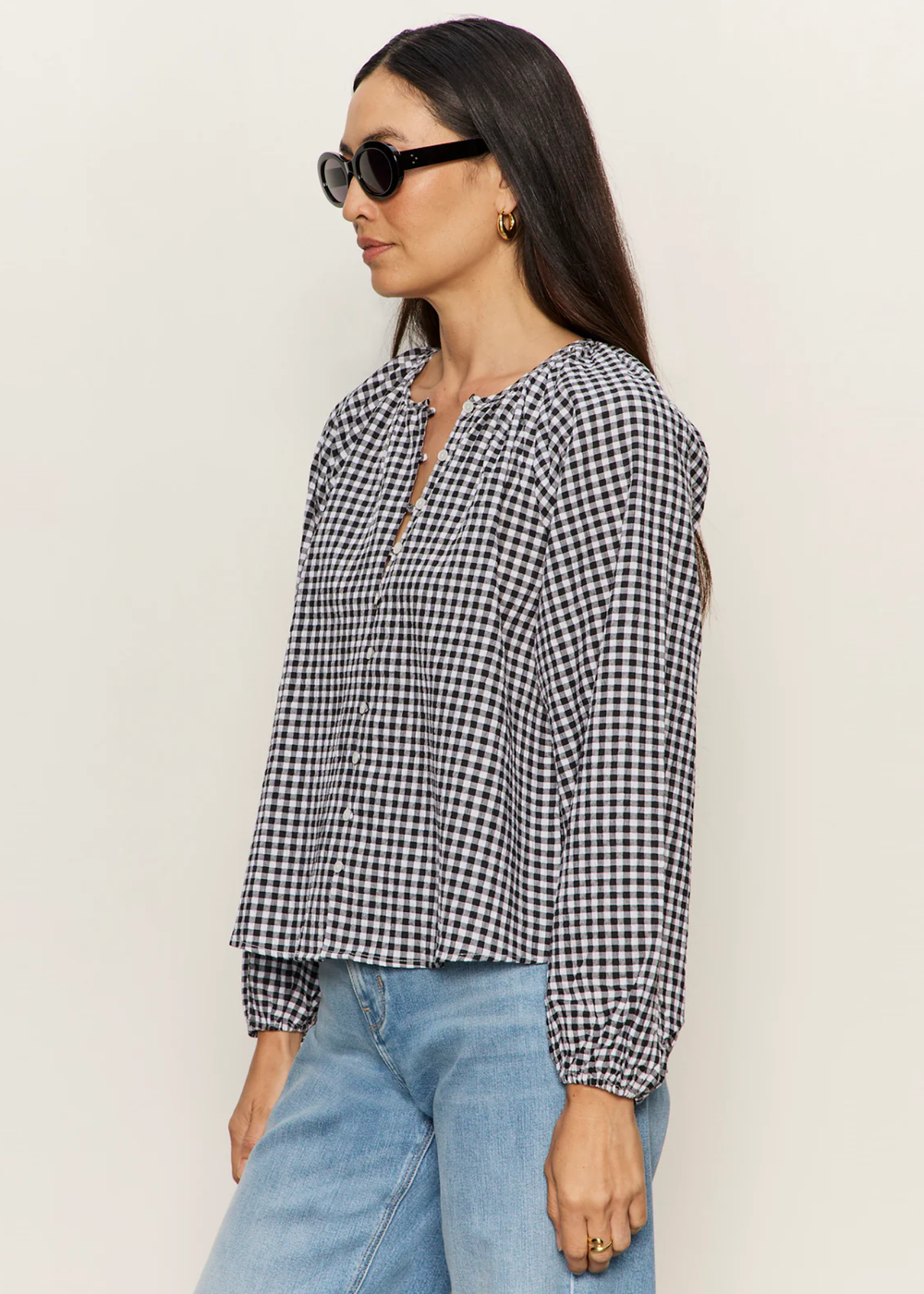 Woman turned to the side wearing a black and white gingham top with jeans