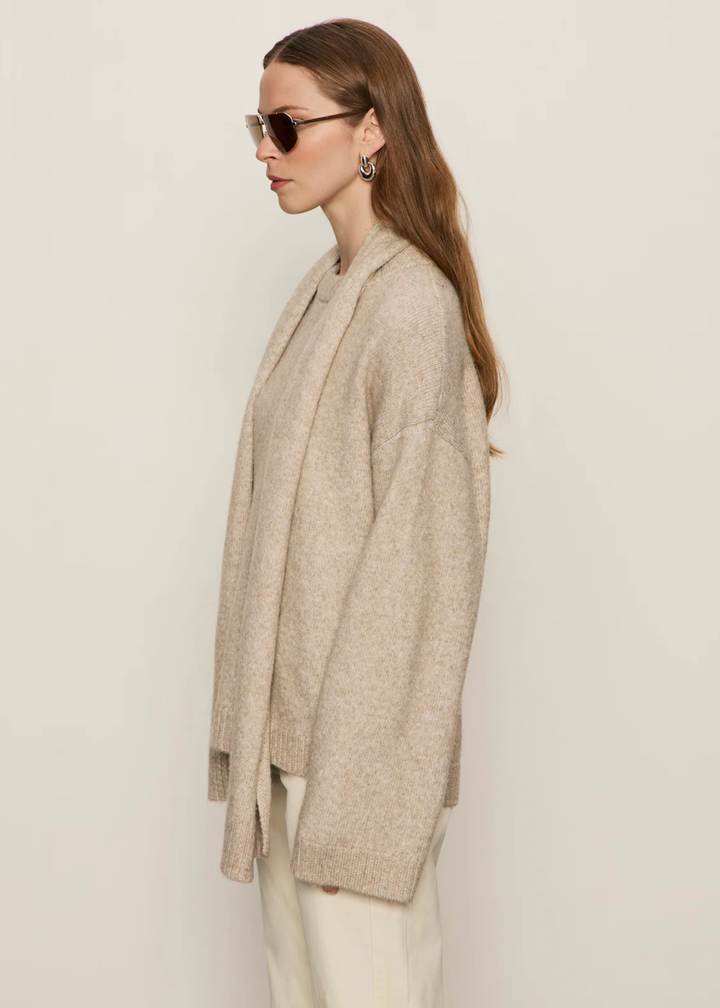 Woman turned to the side wearing a tan sweater with a tan scarf and cream jeans