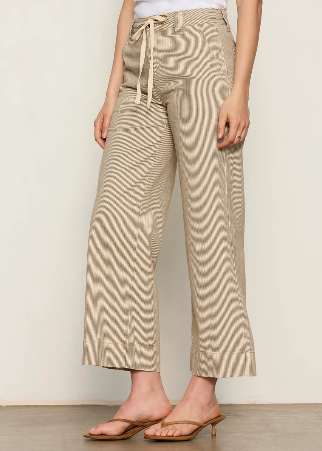 Woman wearing brown and white striped wide leg pants with sandals and a white tank top