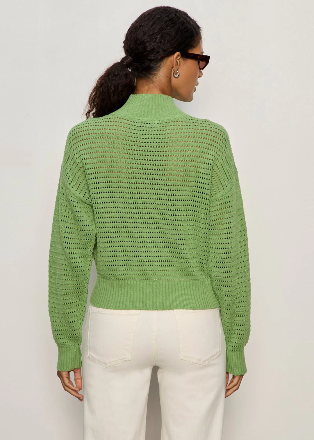 Woman turned around wearing a green knit half zip sweater with cream jeans