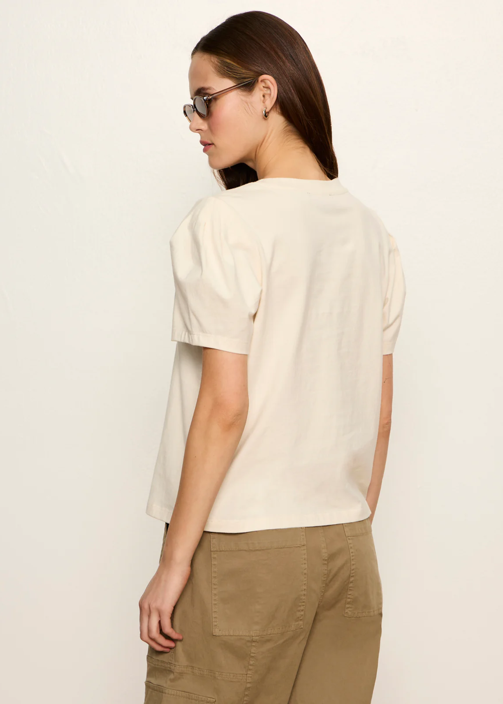 Woman turned around wearing a cream top with tan pants and sunglasses