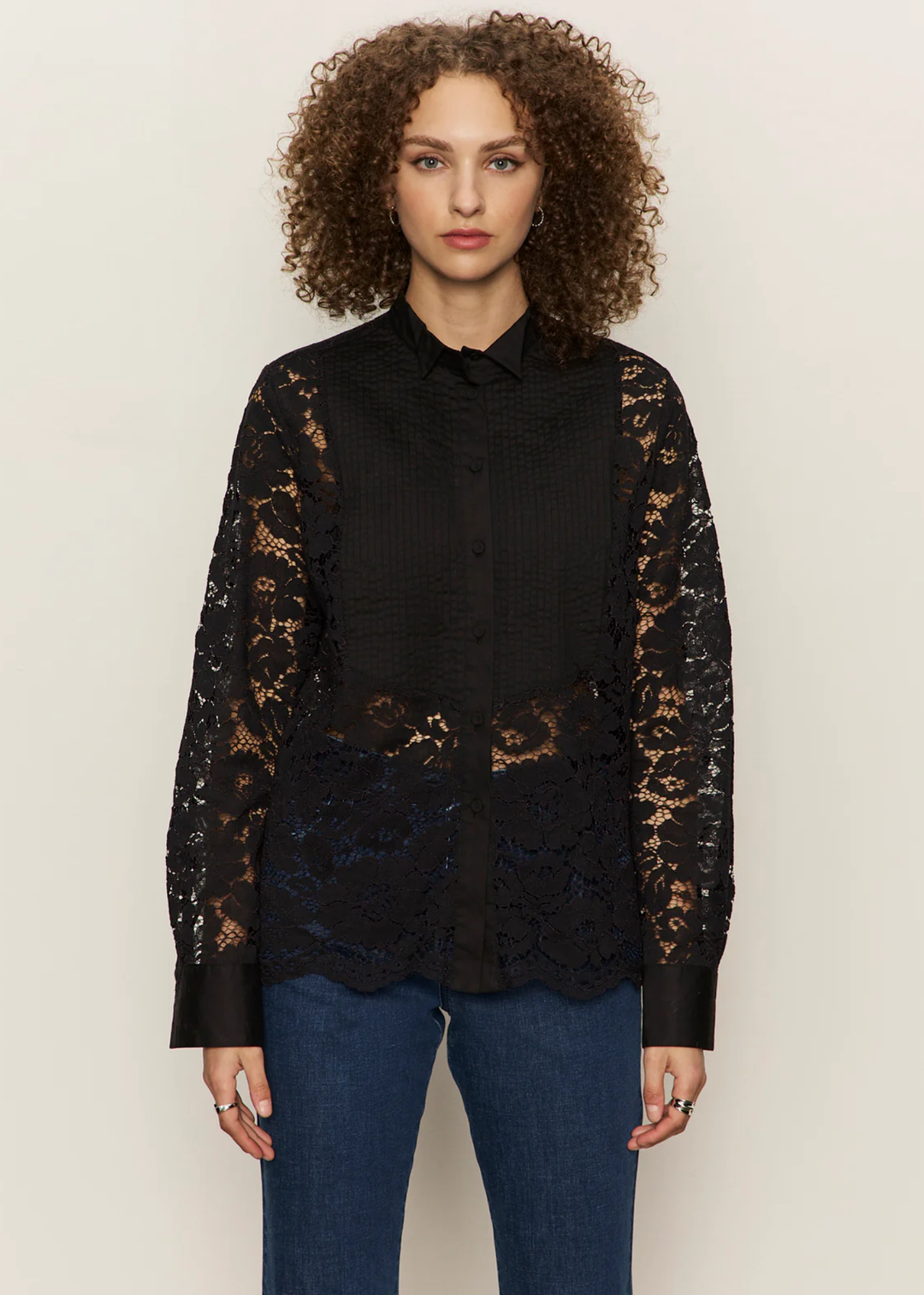 Woman wearing a black button down shirt with lace sleeves and back with jeans against a white background