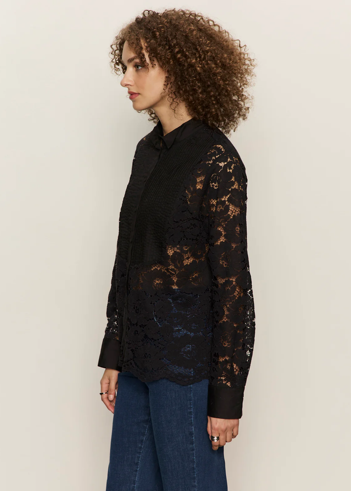 Woman turned to the side wearing a black button down shirt with lace sleeves and back with jeans against a white background