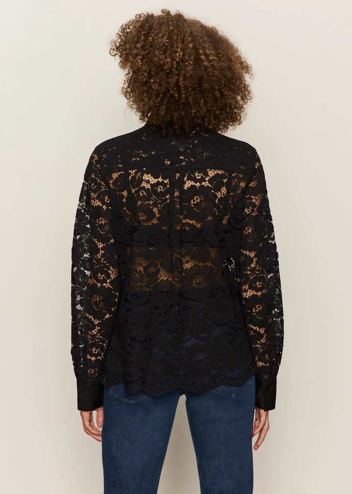 Woman turned around wearing a black button down shirt with lace sleeves and back with jeans against a white background