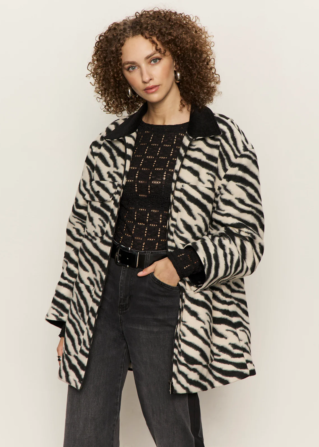 Woman wearing a white and black zebra print barn jacket with black washed jeans against a white background
