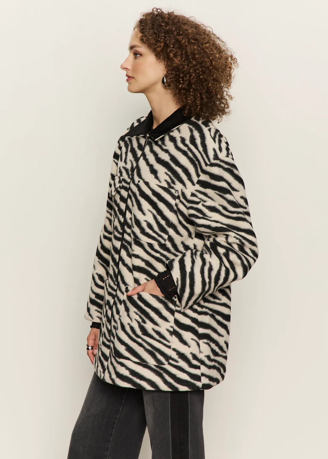 Woman turned to the side wearing a white and black zebra print barn jacket with black washed jeans against a white background