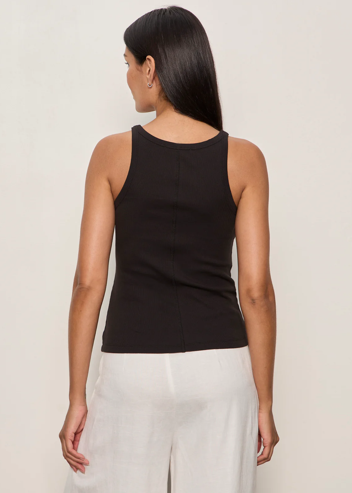 Woman turned around wearing a black tank top with white bottoms and a brown belt