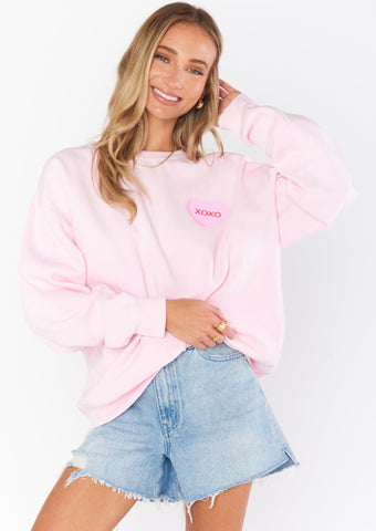 light pink sweatshirt featuring printed valenitne's day heart candy with different sayings like "xoxo" on front left chest and back