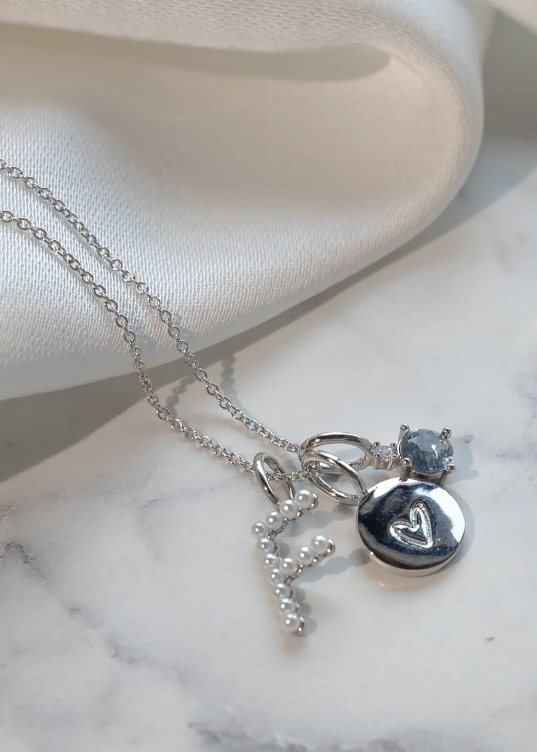 A round silver charm with an engraved heart on a chain necklace with other charms