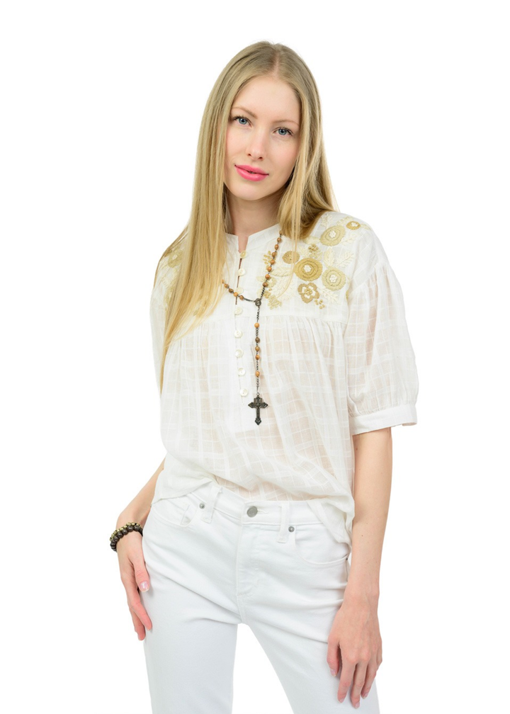 Woman wearing a white top with floral embroidery on the top and white jeans