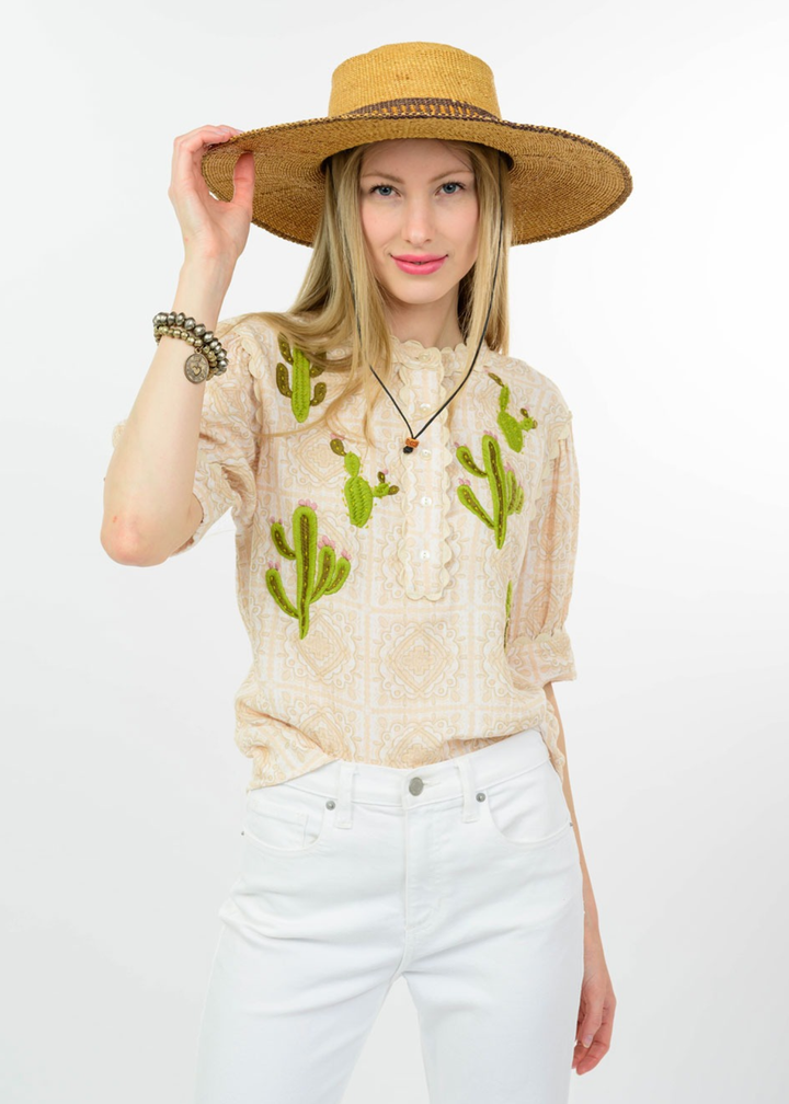 Woman wearing a tan top with cactus embroidery and white jeans