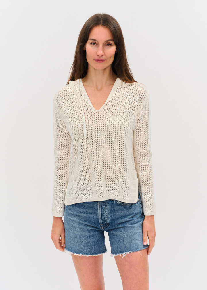 Woman wearing an ivory crochet hoodie with denim shorts