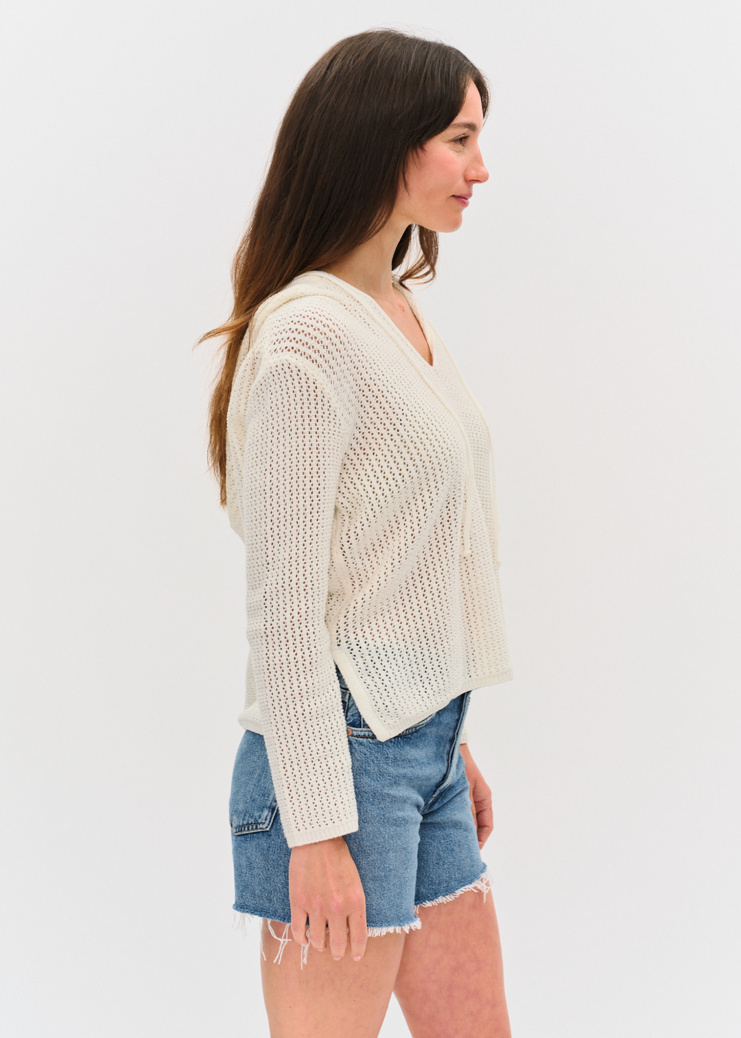 Woman turned to the side wearing an ivory crochet hoodie with denim shorts
