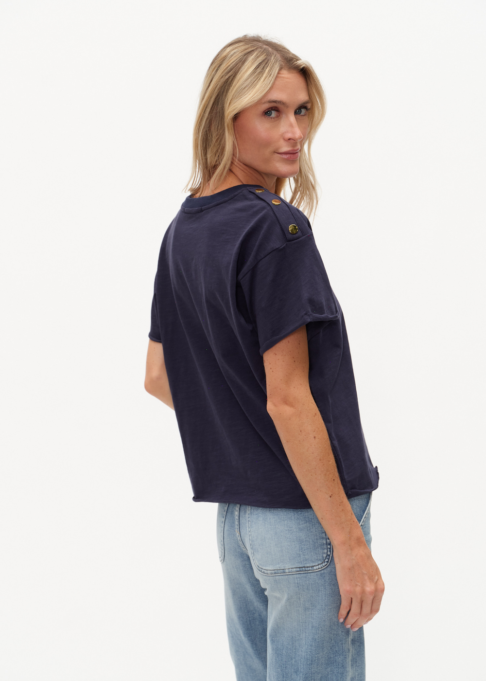 Woman looking over shoulder wearing a navy tee shirt with buttons on the shoulders