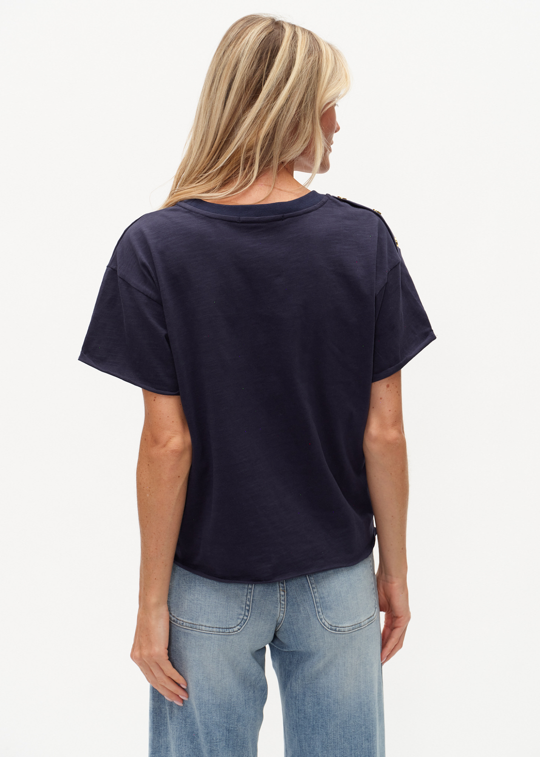 Woman turned around wearing a navy tee shirt with buttons on the shoulders