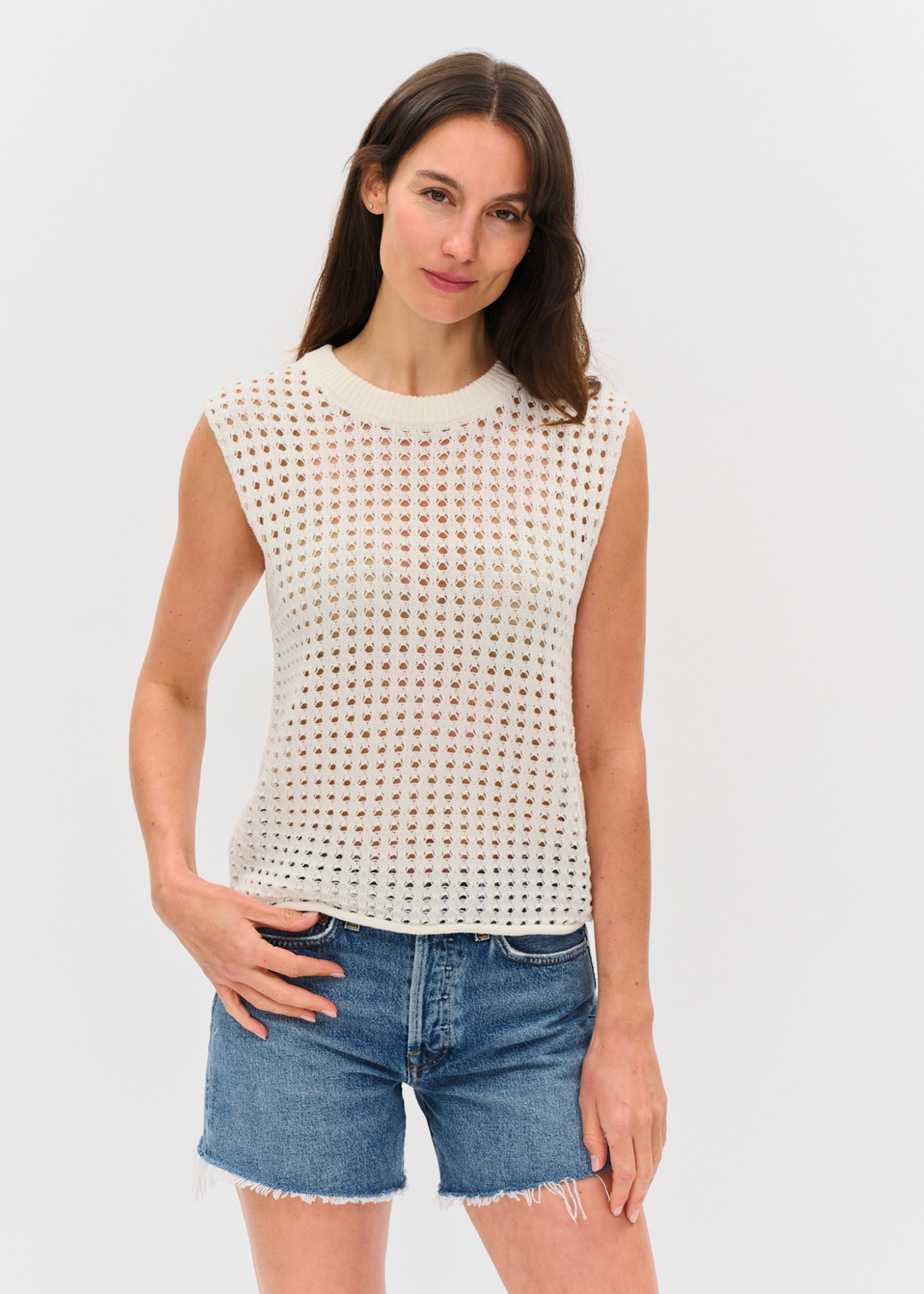 Woman wearing an ivory crochet tank top with denim shorts