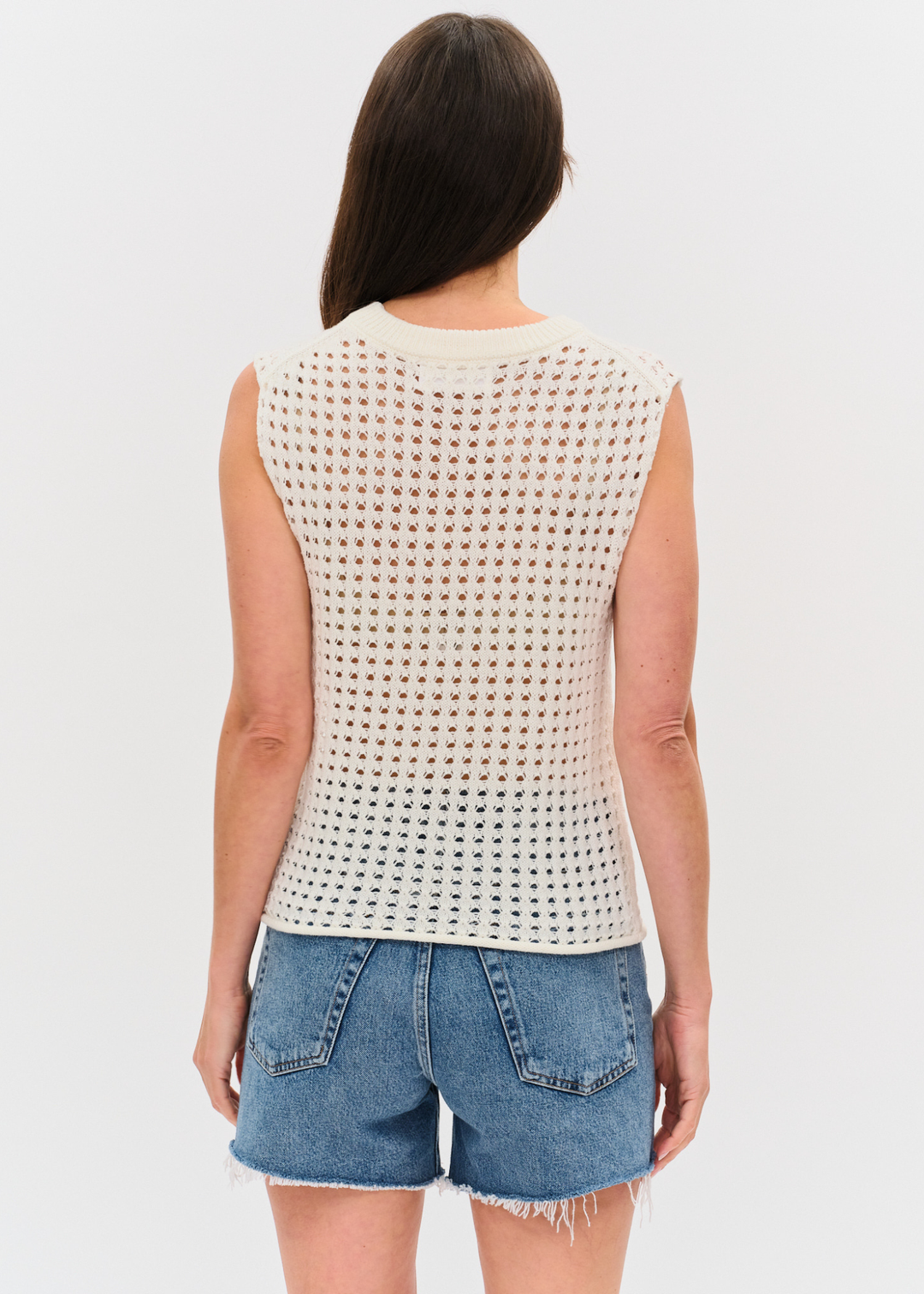 Woman turned around wearing an ivory crochet tank top with denim shorts
