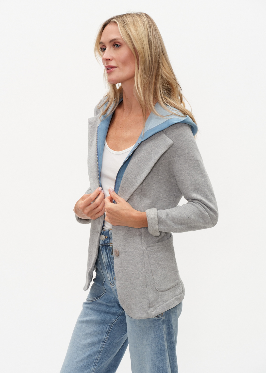 Woman turned to the side wearing a denim and grey knit hooded blazer with jeans